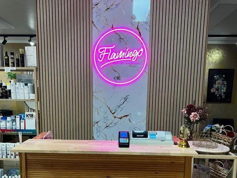 Pink Flamingon logoneonkyltti kauneushoitolan vastaanottotiskin takana