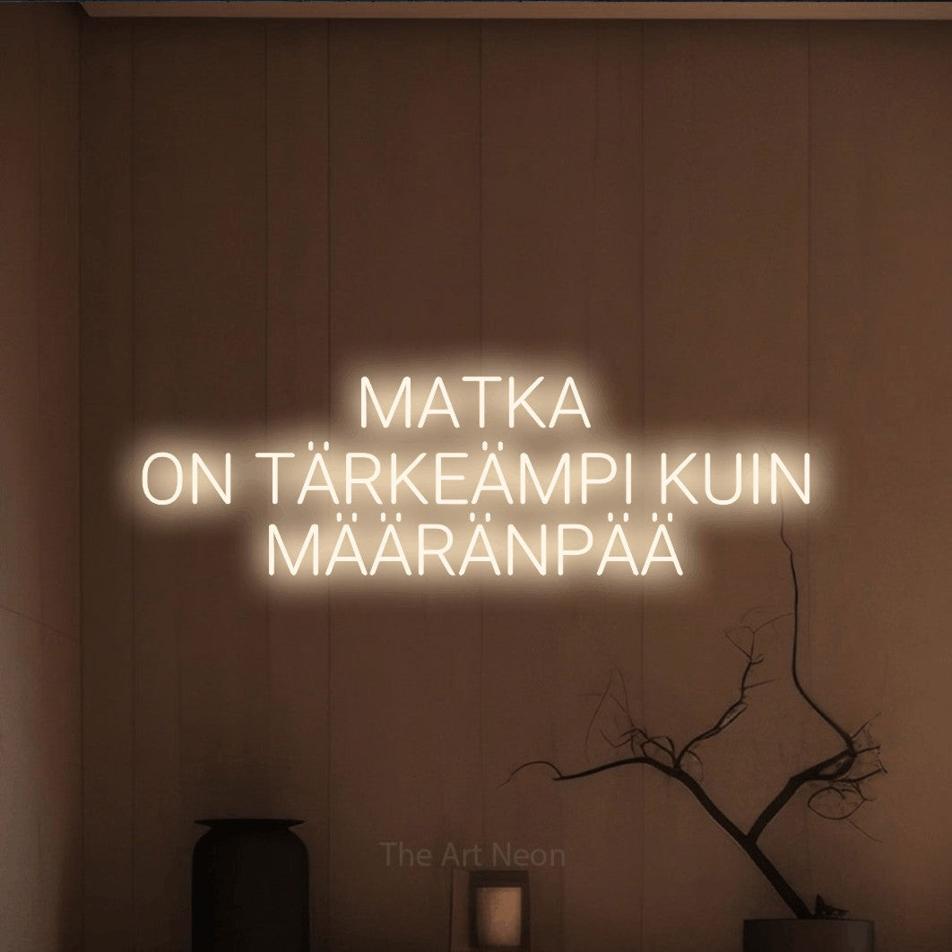 LED neon sign reading “MATKA ON TÄRKEÄMPI KUIN MÄÄRÄNPÄÄ”, arranged in 3 lines.