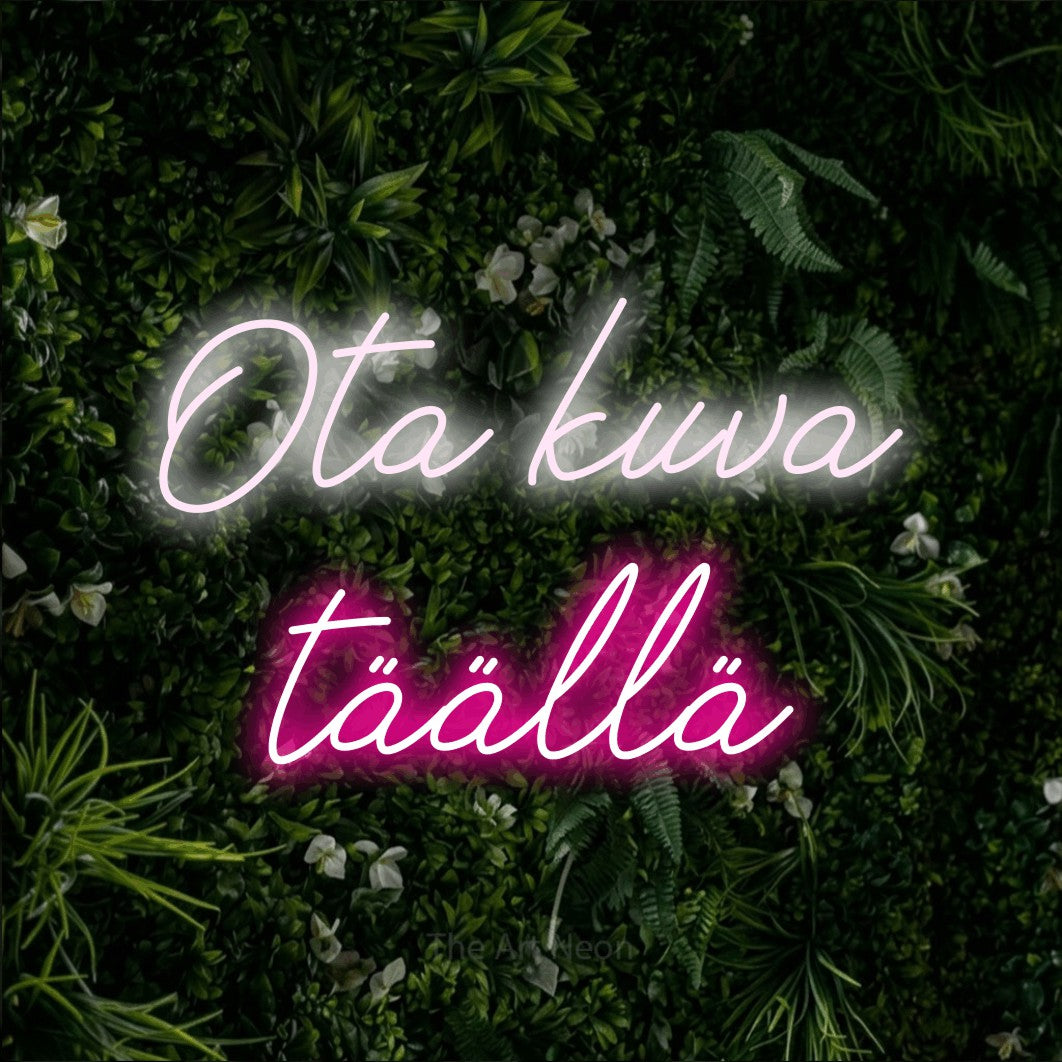LED neon sign reading “Ota kuva täällä”, arranged in 2 lines.