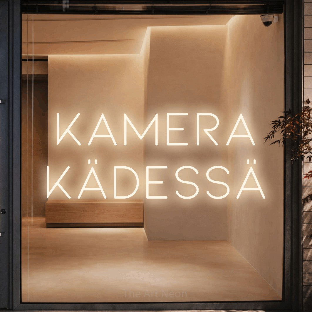LED neon sign reading “kamera kädessä”, arranged in 2 lines.