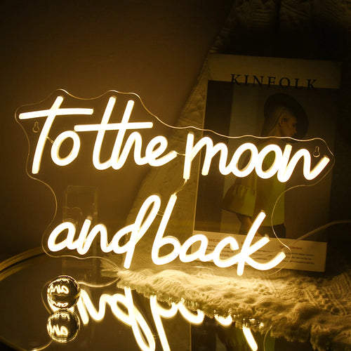 Kuvassa on käsintehty LED-valokyltti, jossa on teksti "To The Moon And Back" eleganteilla, kursiivisilla kirjaimilla.