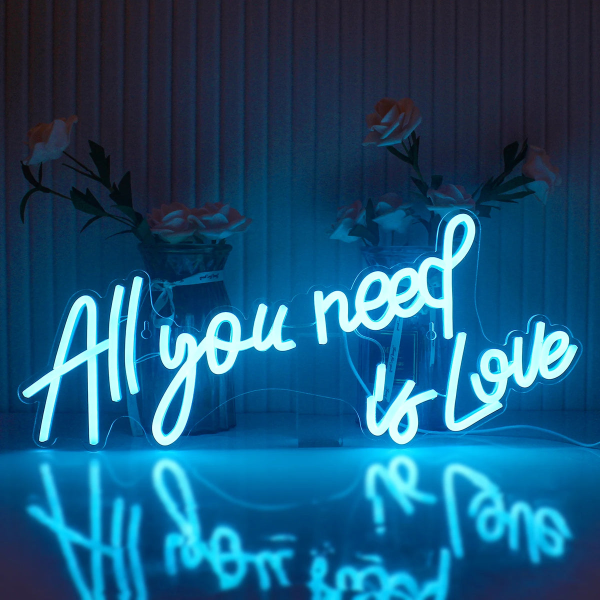 Kuvassa näkyy eloisa LED-valokyltti, joka kirjoittaa ilmauksen "All You Need Is Love" tyylikkäällä kursiivilla fontilla.