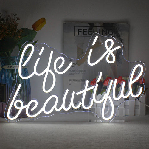 Kuvassa on eloisa, hehkuva LED-neonkyltti, jossa näkyy sana "Life is Beautiful" kursiivisella fontilla.