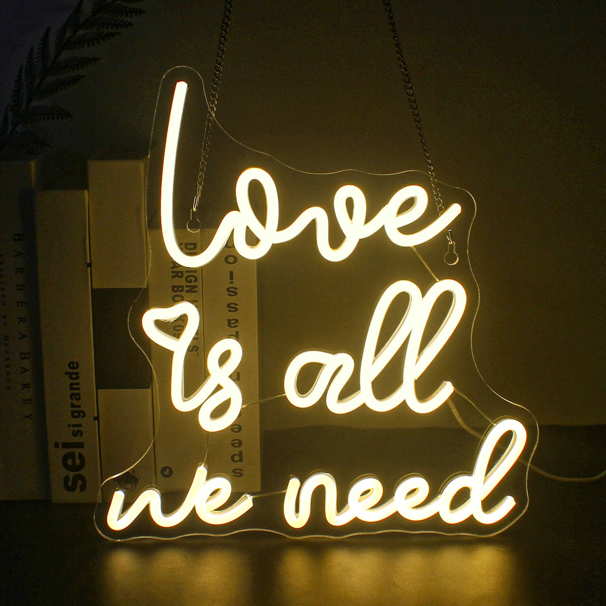 Kuvassa on eloisa LED-valokyltti, jossa lukee "Love is all we need" virtaavalla, kursiivisella fontilla.