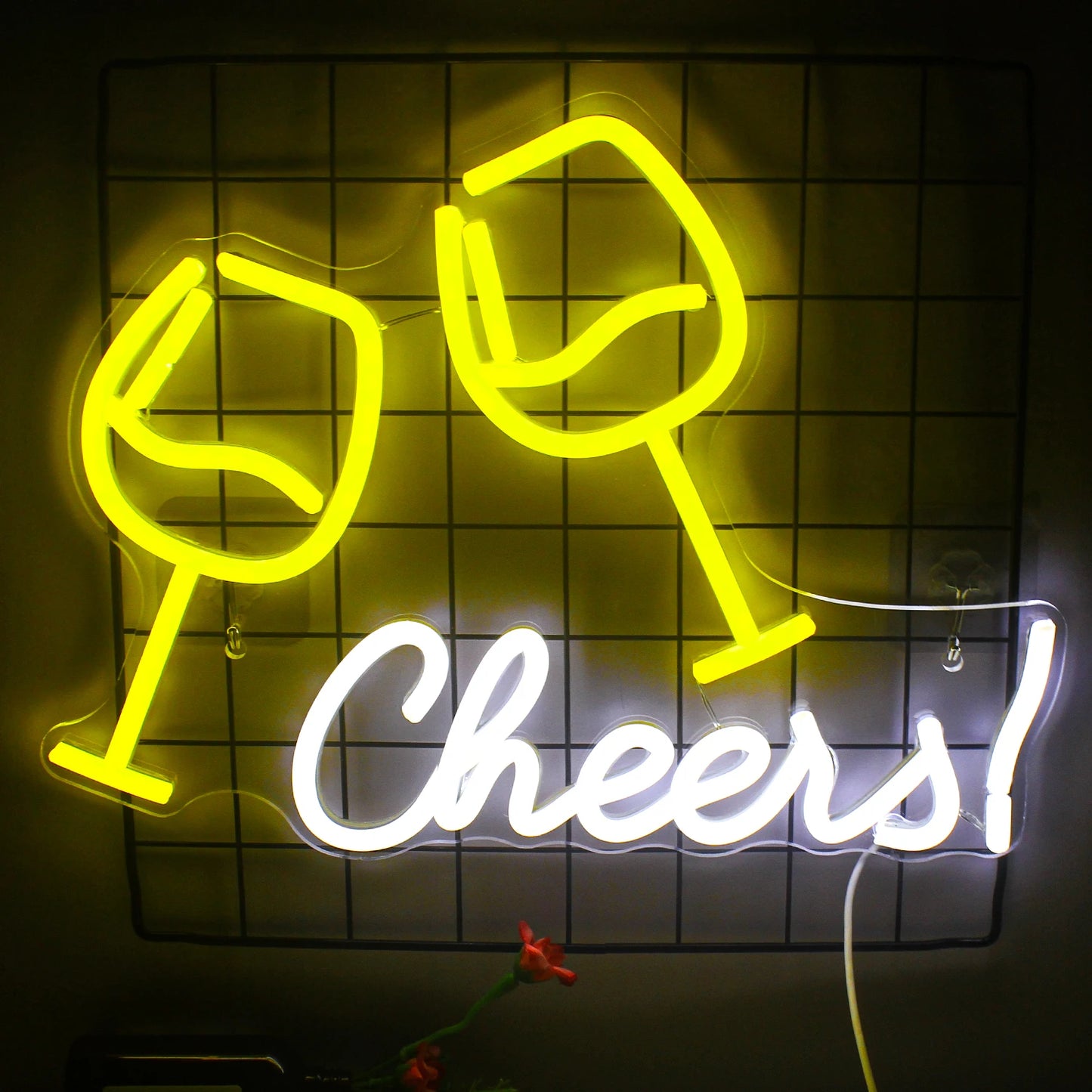 A vibrant LED neon sign reading "Cheers" in a playful cursive font is mounted against a brick wall.