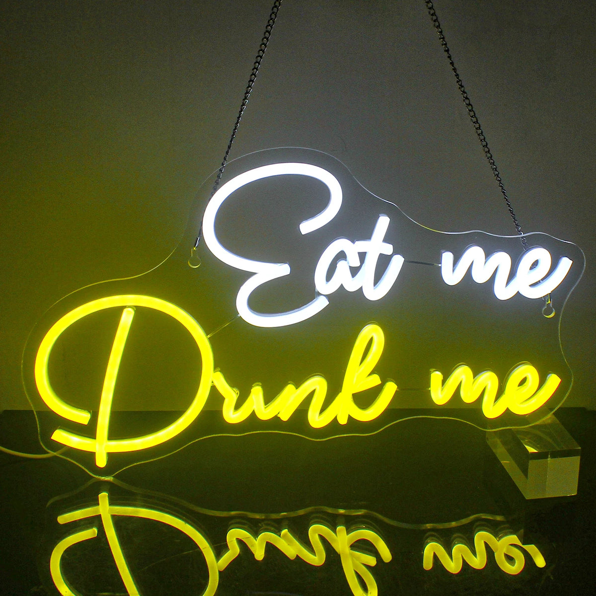 Kuvassa on eloisa LED-valokyltti, jossa on sanat "Eat Me Drink Me" hassulla kursiivilla fontilla.