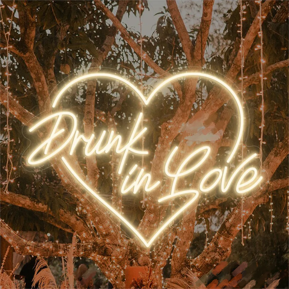 Kuvassa on tyylikäs LED-valokyltti, joka kirjoittaa lauseen "Drunk in Love" kirkkaalla, hehkuvalla kursiivilla fontilla.
