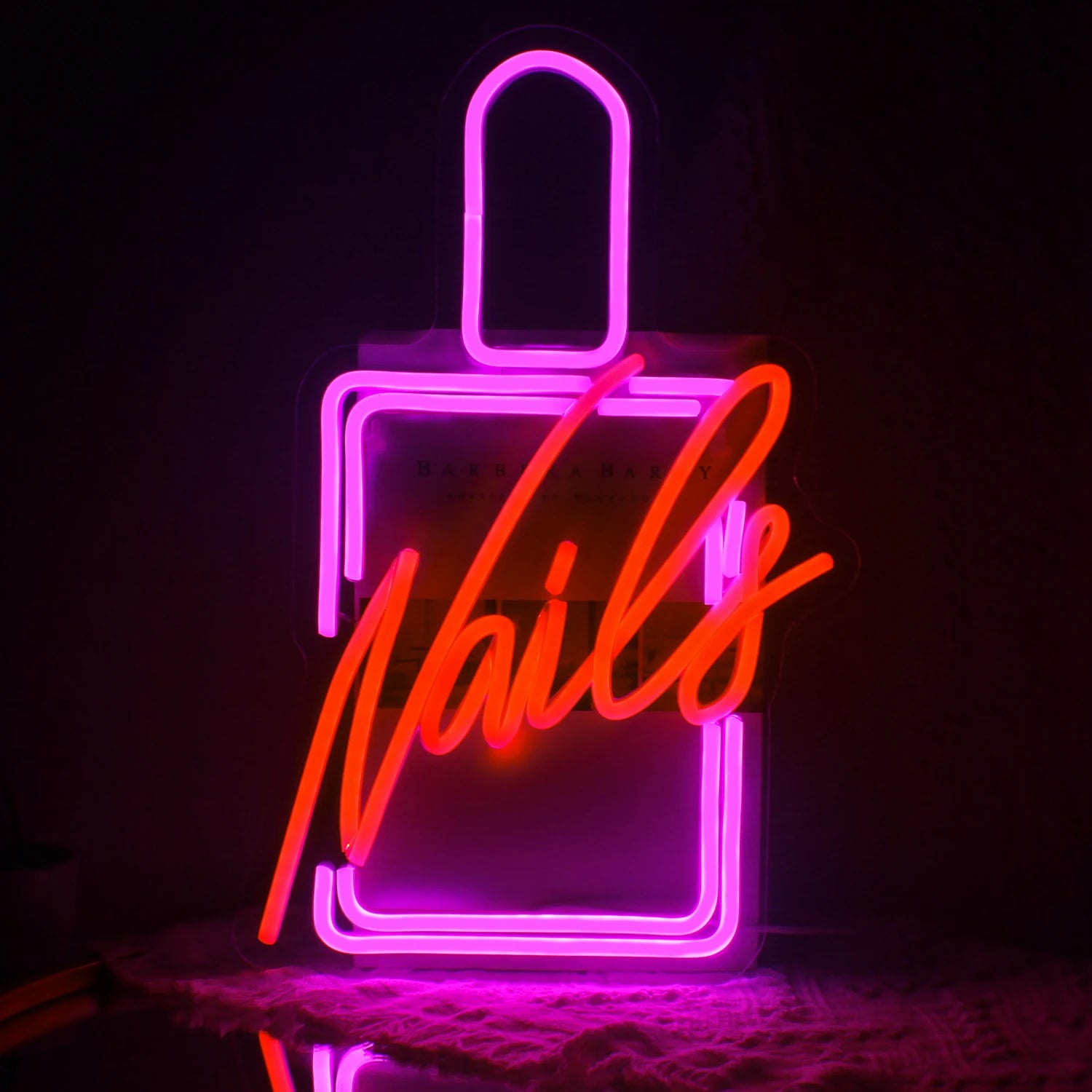 The image features a vibrant LED neon sign that spells out the word "Nails" in a stylish cursive font.