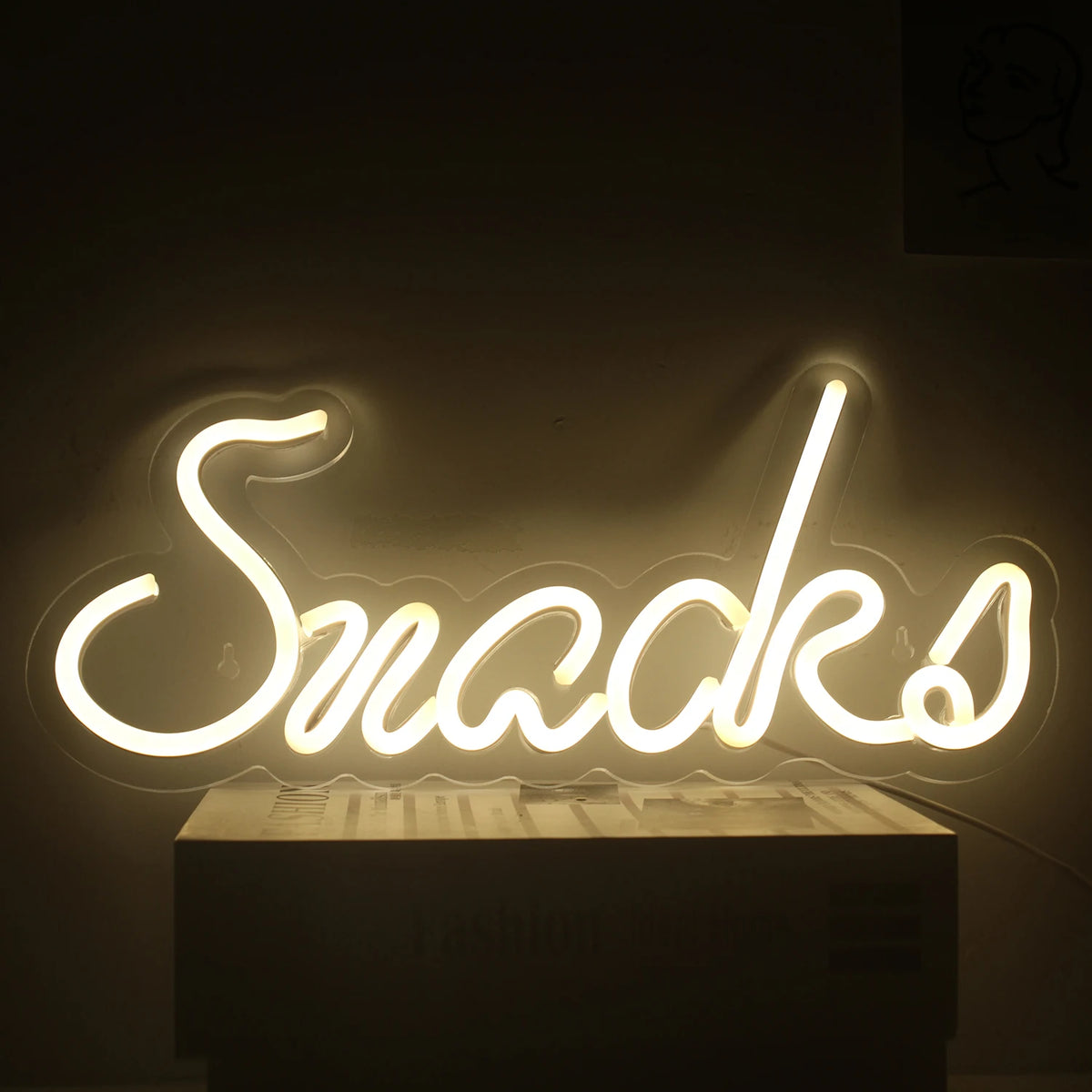 Kuvassa on eloisa LED-neonkyltti sanan "Snacks" muodossa leikkisällä, kursiivisella fontilla.
