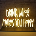 Kuvassa on eloisa LED-valokyltti, jossa on teksti "Drink What Makes You Happy" tyylikkäällä kursiivikirjasimella.