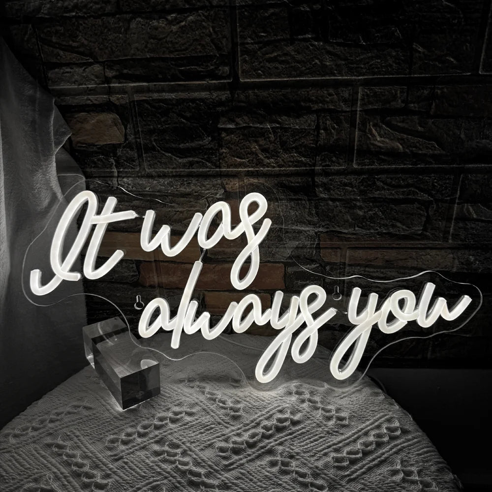 Kuvassa on eloisa LED-valokyltti, jossa näkyvät sanat "It Was Always You" tyylikkäällä kursiivisella fontilla.
