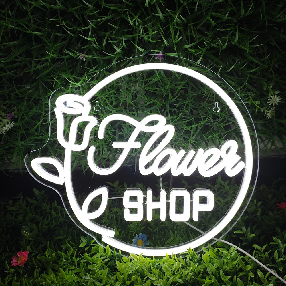 The image features a vibrant LED neon sign that reads "Flower Shop" in elegant script.