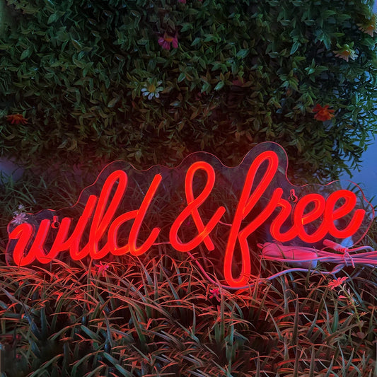 The image features a vibrant LED neon sign displaying the words "Wild & Free" in a stylish, cursive font.