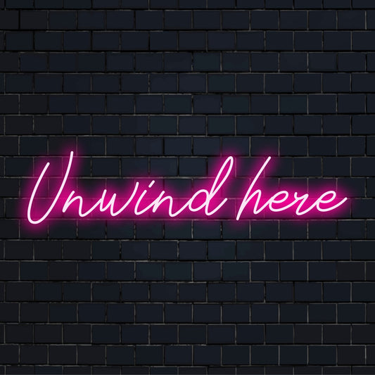 Custom LED neon sign reading Unwind Here; perfect neon wall art for creating a relaxing atmosphere.