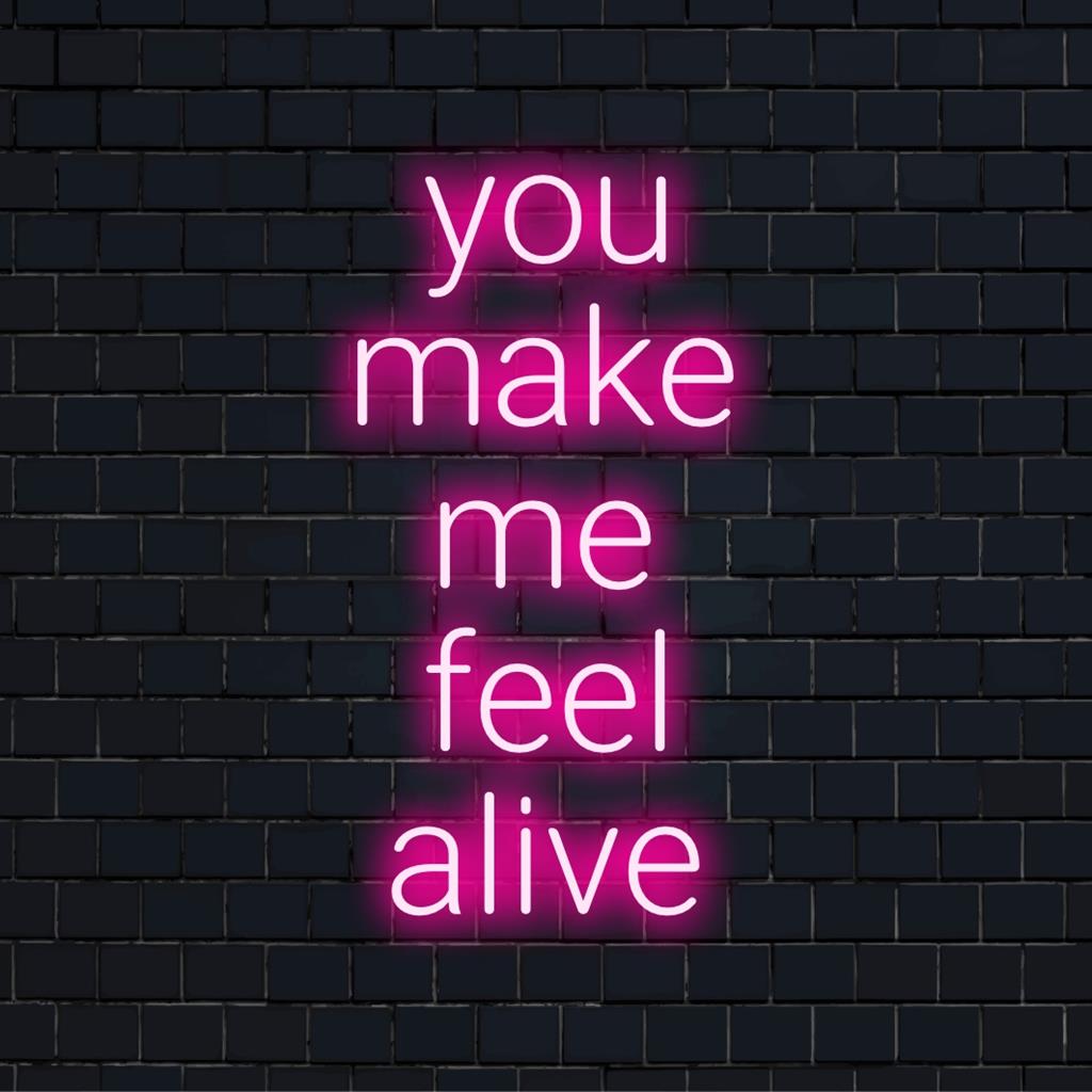Mukautettu LED-neonkylttikirjoitus You Make Me Feel Alive lihavoituina, hehkuen eloisin värein tummaa taustaa vasten.