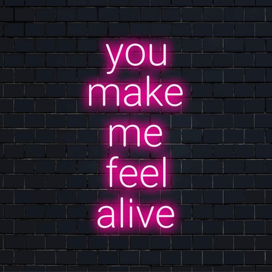 Mukautettu LED-neonkylttikirjoitus You Make Me Feel Alive lihavoituina, hehkuen eloisin värein tummaa taustaa vasten.