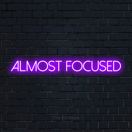 "Almost Focused" neon text design on a black brick wall