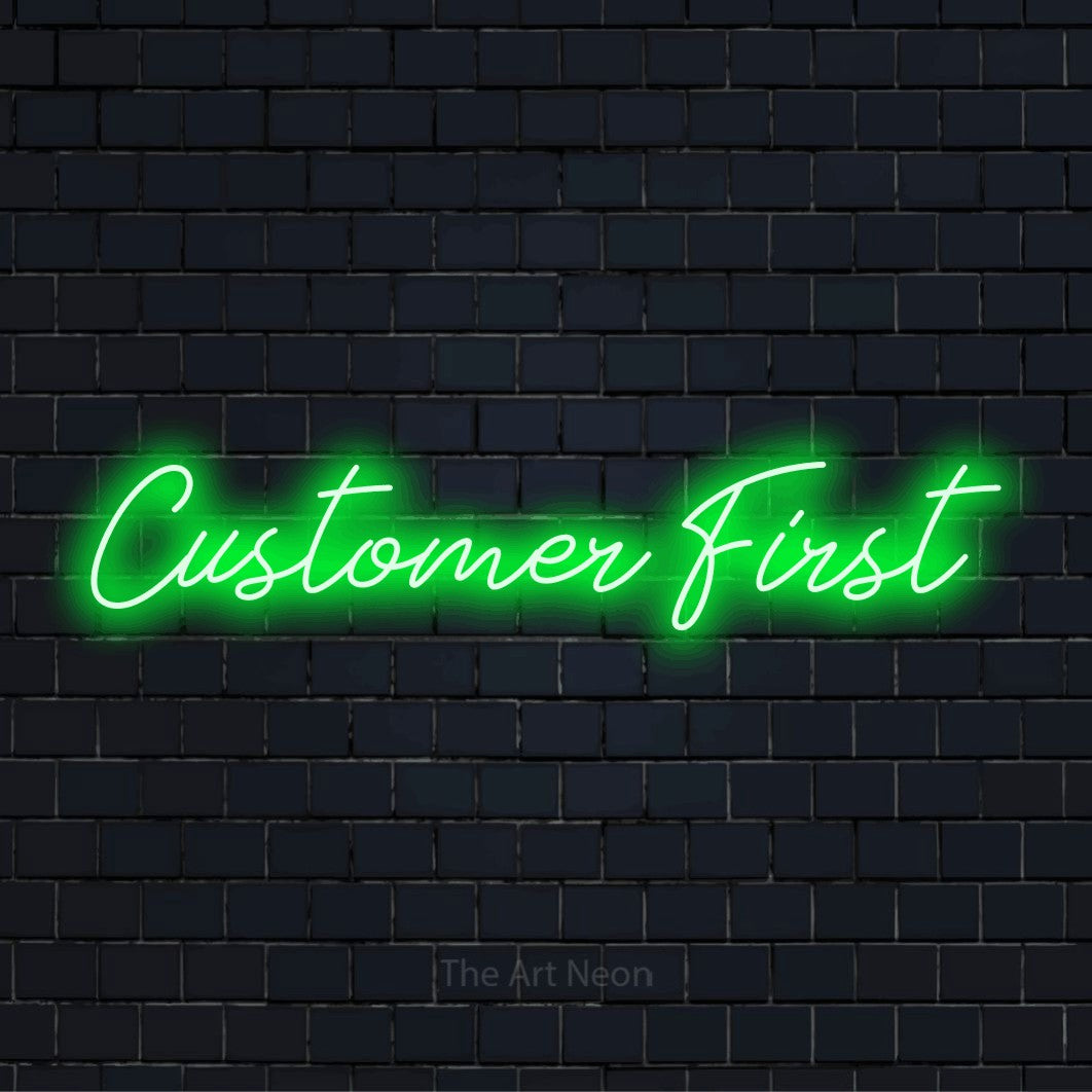 "Customer First" script-style LED neon sign on a black brick wall