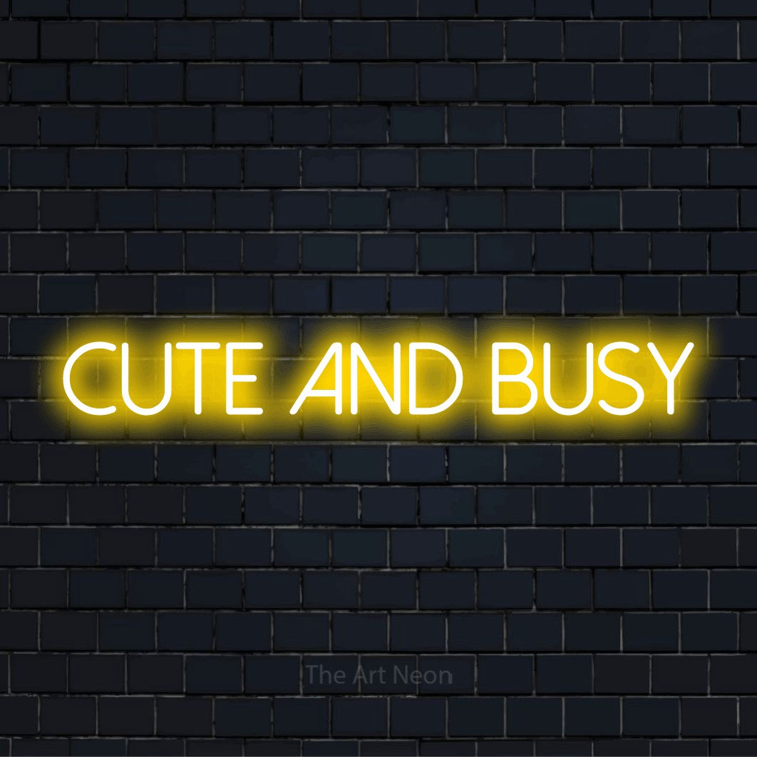 "Cute And Busy" script-style LED neon sign on a black brick wall