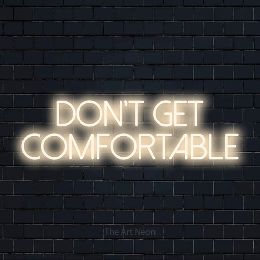 "Don’t Get Comfortable" neon text design on a black brick wall
