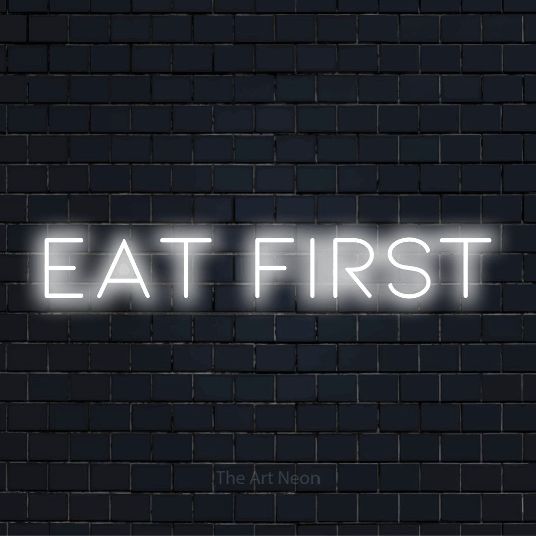 "Eat First" script-style LED neon sign on a black brick wall