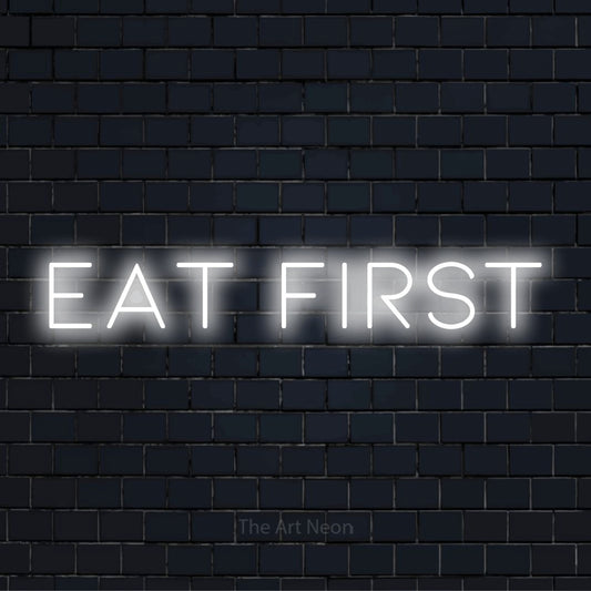 "Eat First" script-style LED neon sign on a black brick wall