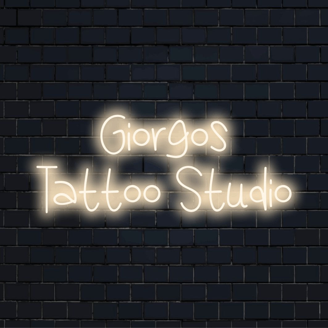 Giorgos Tattoo Studio Custom Name Neon Sign, glowing lettering on dark brick background