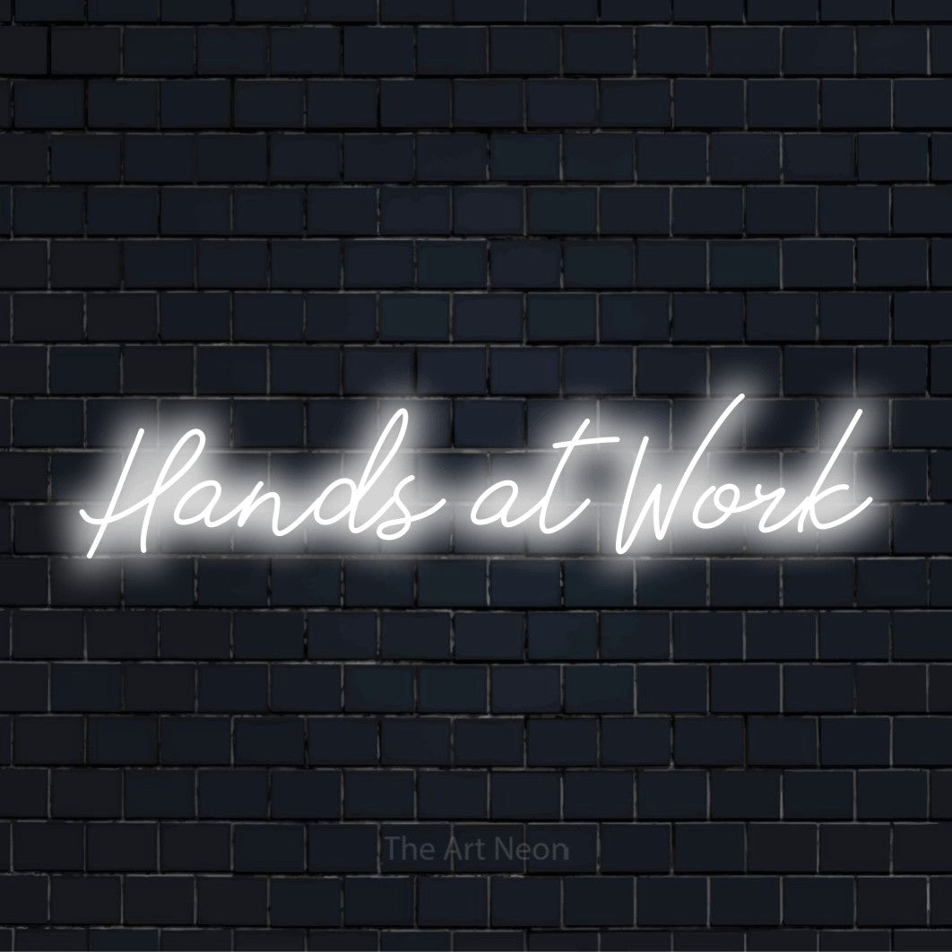 "Hands At Work" script-style LED neon sign on a black brick wall