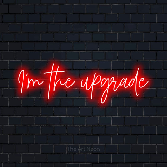 "I’m The Upgrade" script-style LED neon sign on a black brick wall