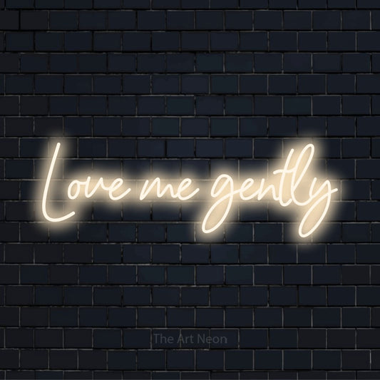 "Love Me Gently" text design with neon effect on a black brick wall