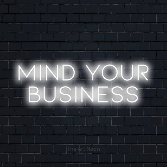 "Mind Your Business" script-style LED neon sign on a black brick wall