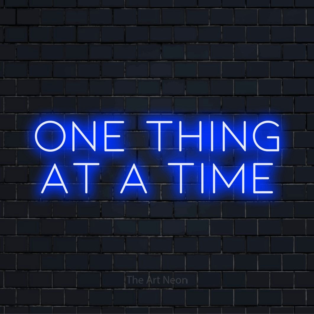 "One Thing At A Time" LED neon sign on a black brick wall
