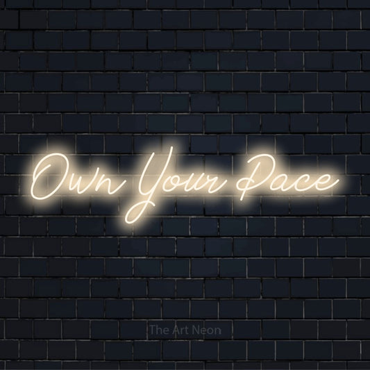 "Own Your Pace" glowing LED neon sign on a black brick wall