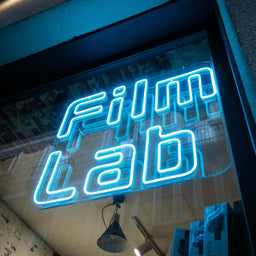 Neon sign reading 'Film Lab' inside a building with a textured wall.
