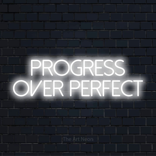 "Progress Over Perfect" script-style LED neon sign on a black brick wall