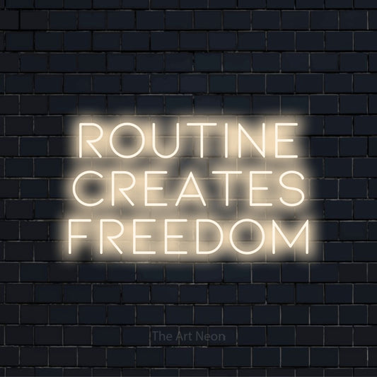 "Routine Creates Freedom" neon text design on a black brick wall