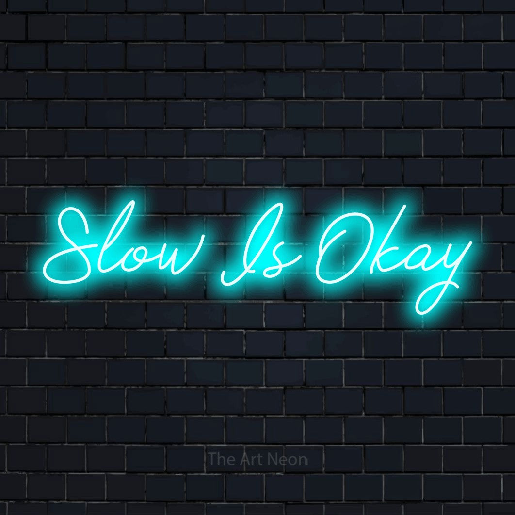 "Slow Is Okay" script-style LED neon sign on a black brick wall