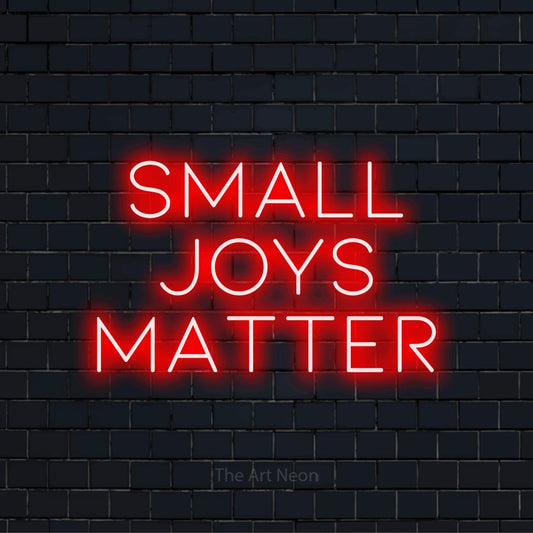 "Small Joys Matter" glowing LED neon sign on a black brick wall