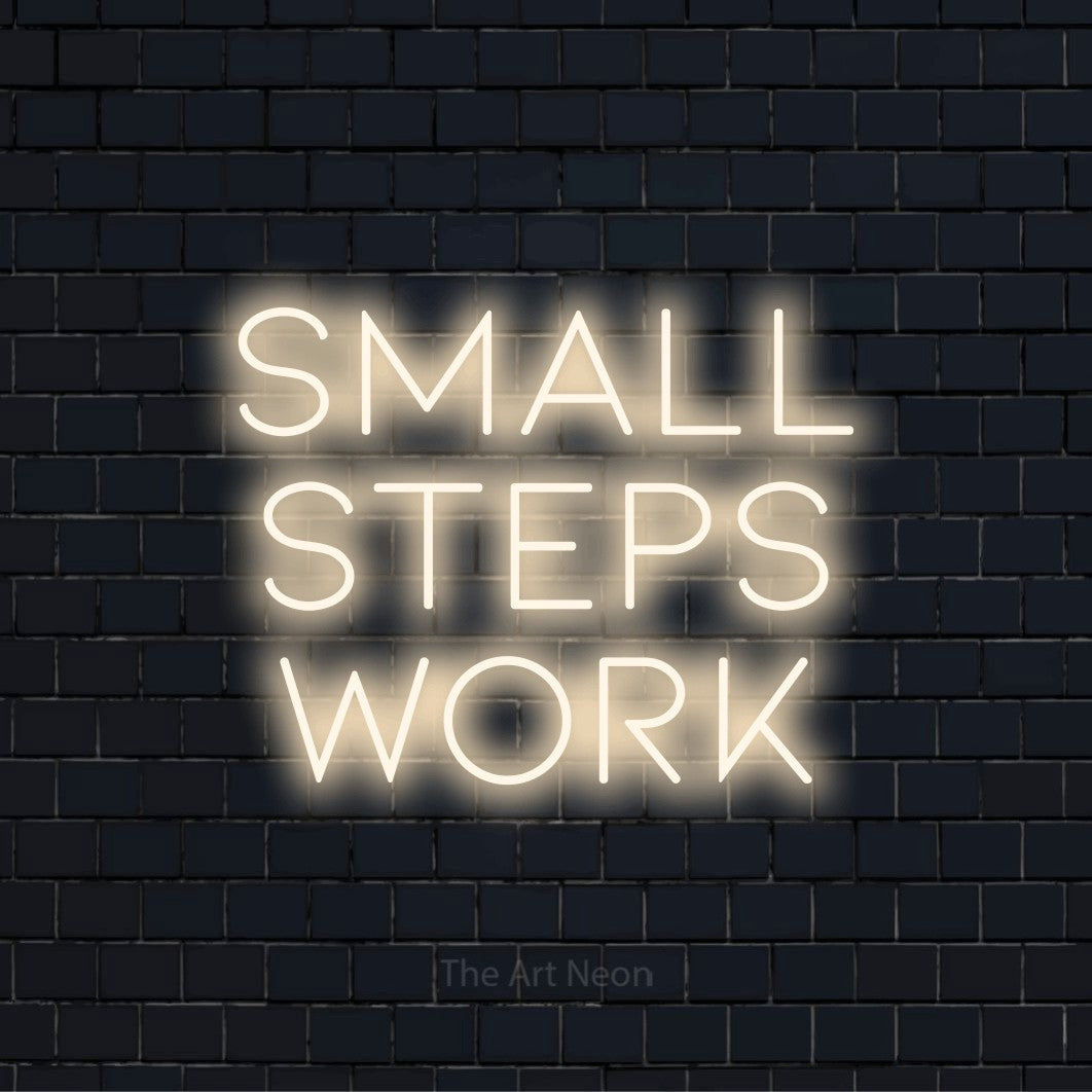 "Small Steps Work" script-style LED neon sign on a black brick wall