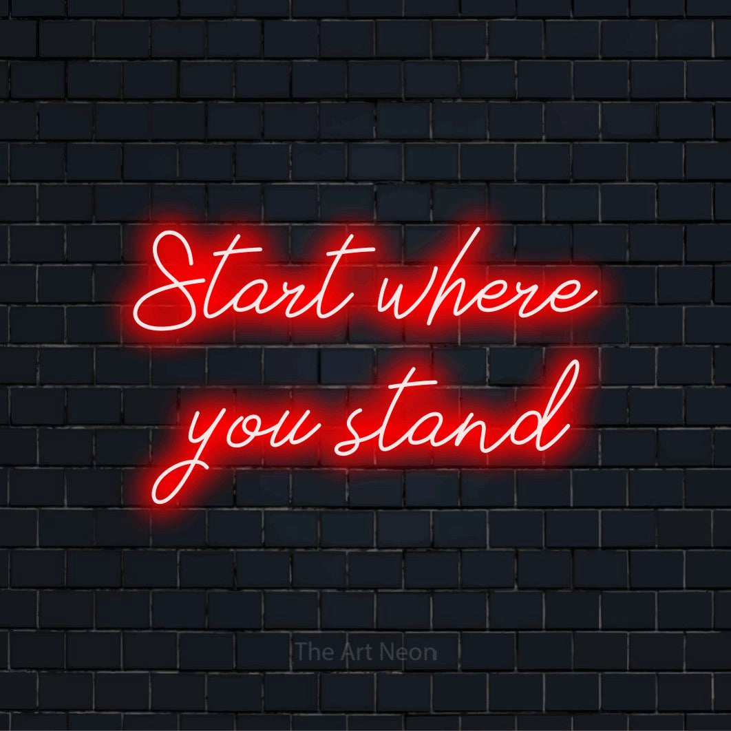 "Start Where You Stand" glowing LED neon sign on a black brick wall