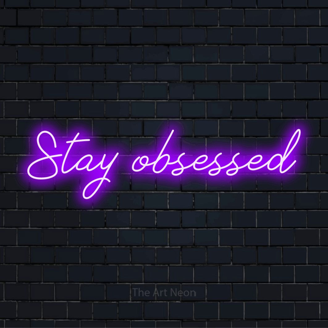 "Stay Obsessed" text design with neon effect on a black brick wall