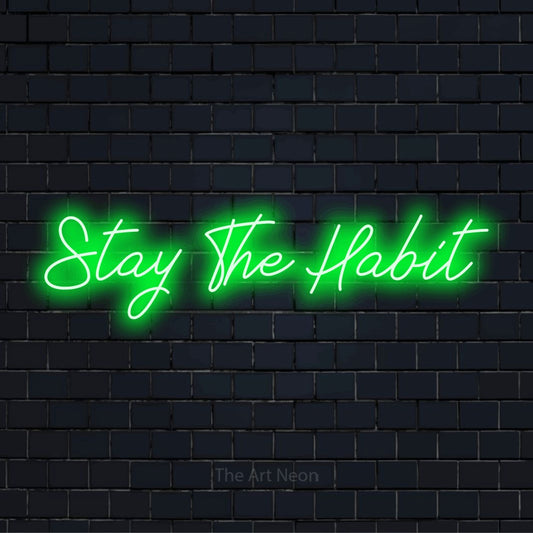 "Stay The Habit" glowing LED neon sign on a black brick wall