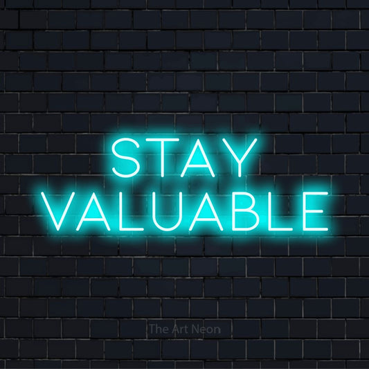 "Stay Valuable" script-style LED neon sign on a black brick wall