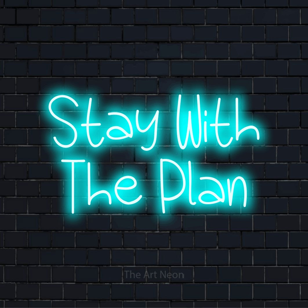 "Stay With The Plan" script-style LED neon sign on a black brick wall