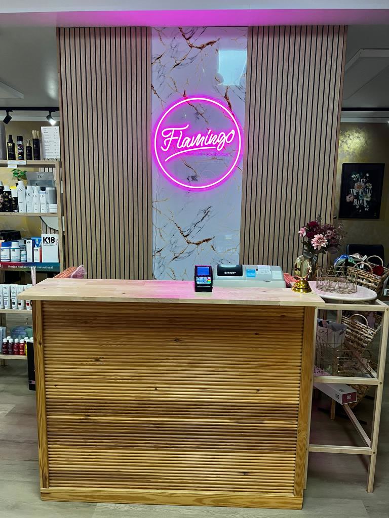 Pink Flamingo logo neon sign installed behind the reception desk at Parturi-Kampaamo Flamingo