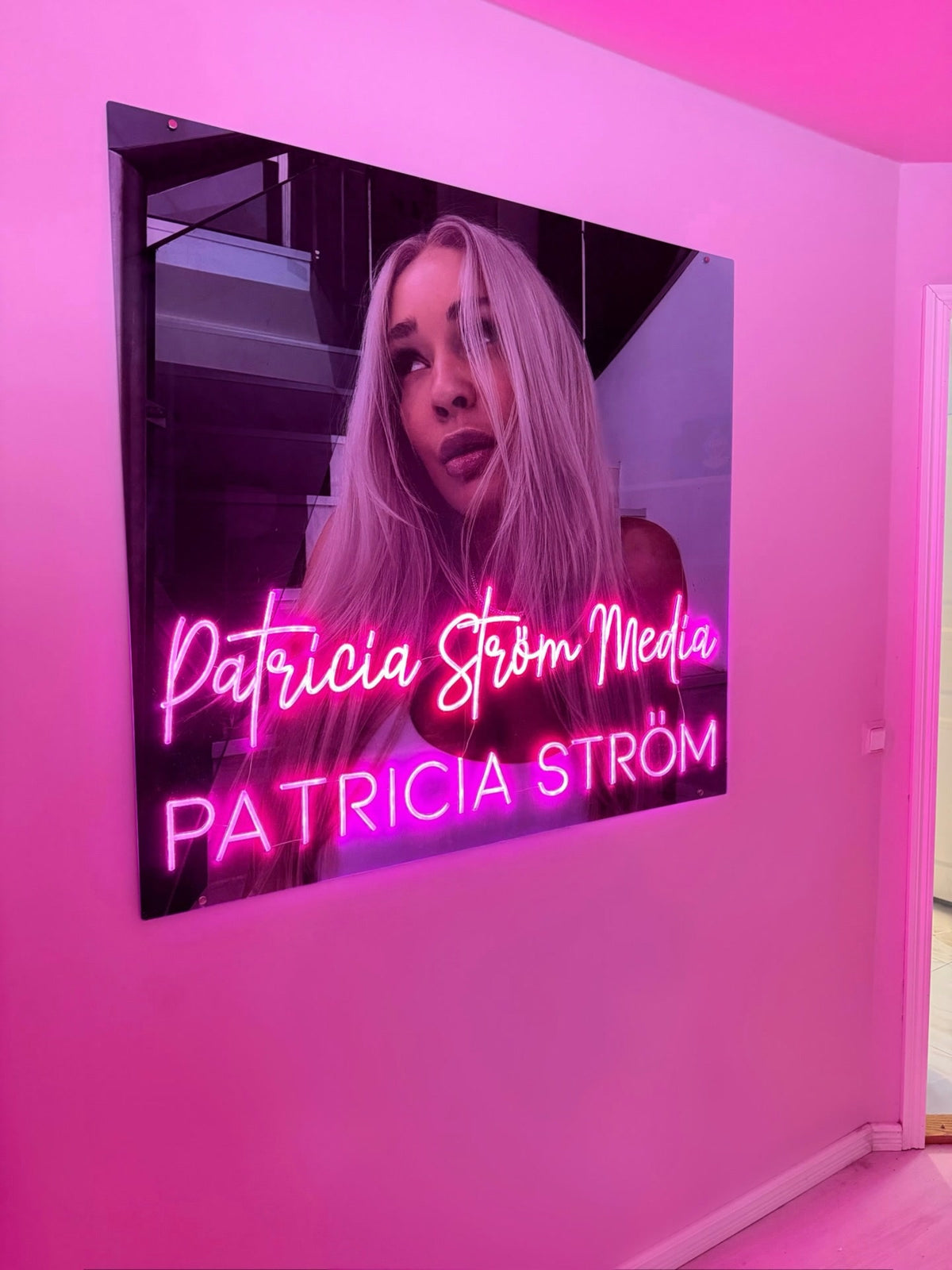 Pinkki Patricia Ström Media -neonlogo Patricia Strömin vieressä hänen brändinsä mukaisessa työtilassa