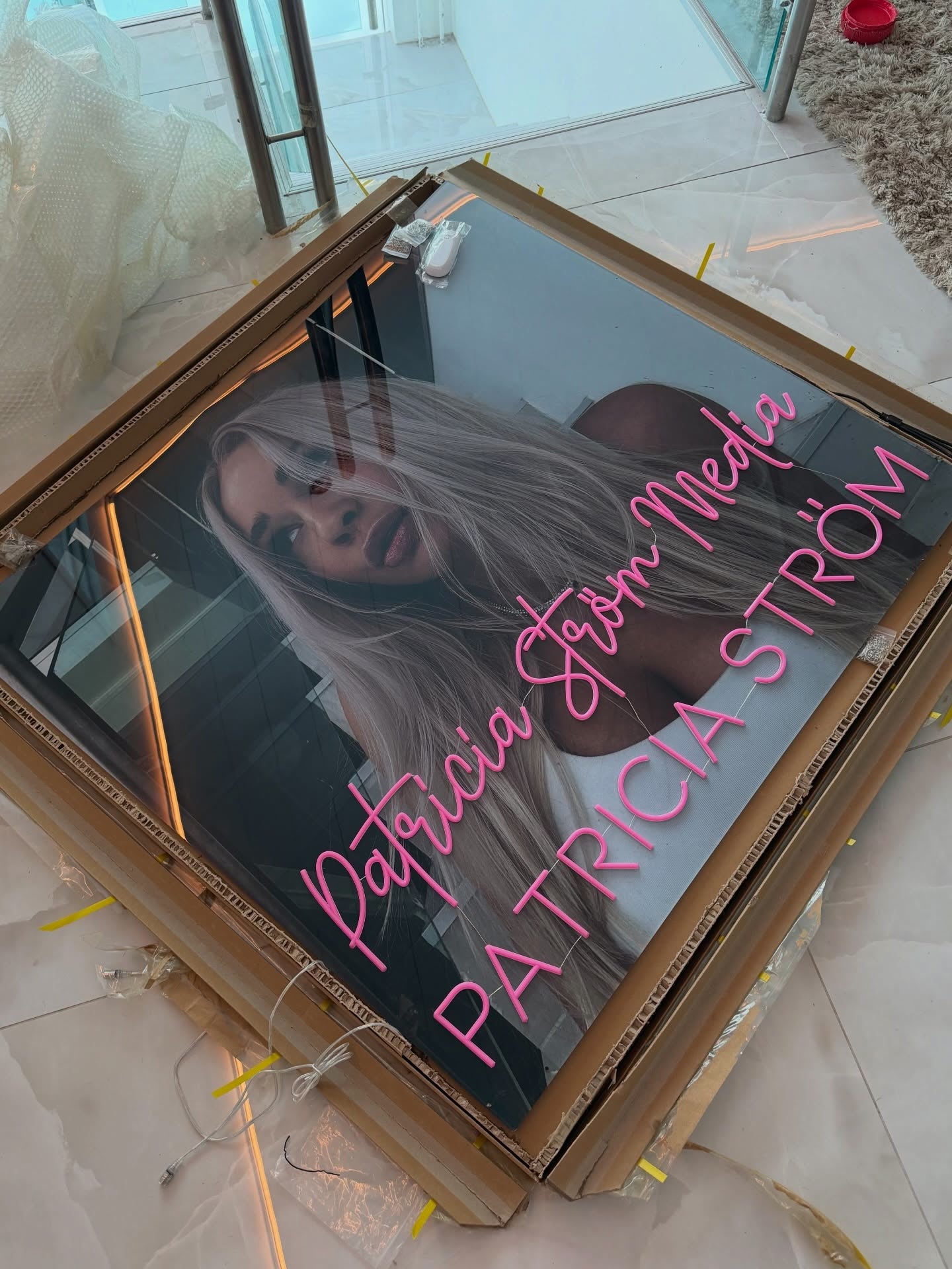 Pink Patricia Ström Media neon logo displayed beside Patricia Ström in her branded workspace