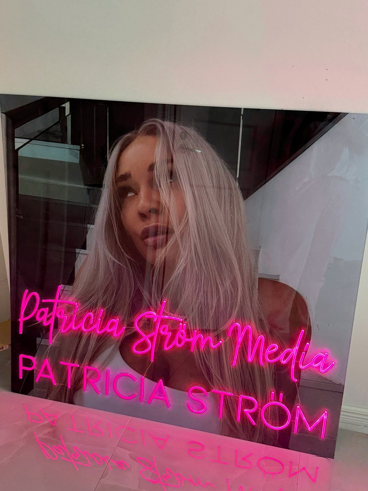 Pinkki Patricia Ström Media -neonlogo Patricia Strömin vieressä hänen brändinsä mukaisessa työtilassa