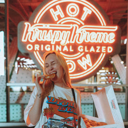 Person eating a donut in front of a neon sign.