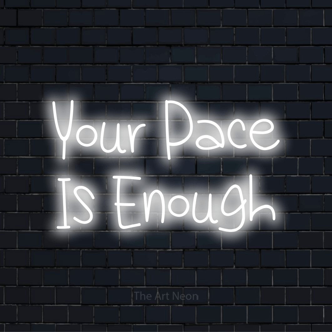 "Your Pace Is Enough" script-style LED neon sign on a black brick wall